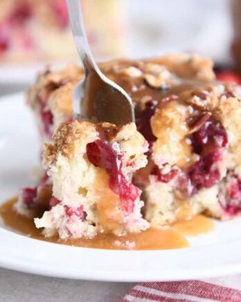 fork taking bite of cranberry coffee cake and warm vanilla sauce