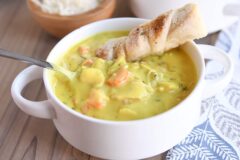 creamy chicken soup in white bowl with spoon and breadstick