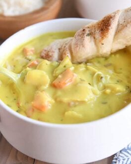 creamy chicken soup in white bowl with spoon and breadstick