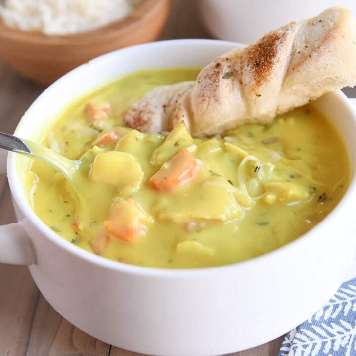 creamy chicken soup in white bowl with spoon and breadstick