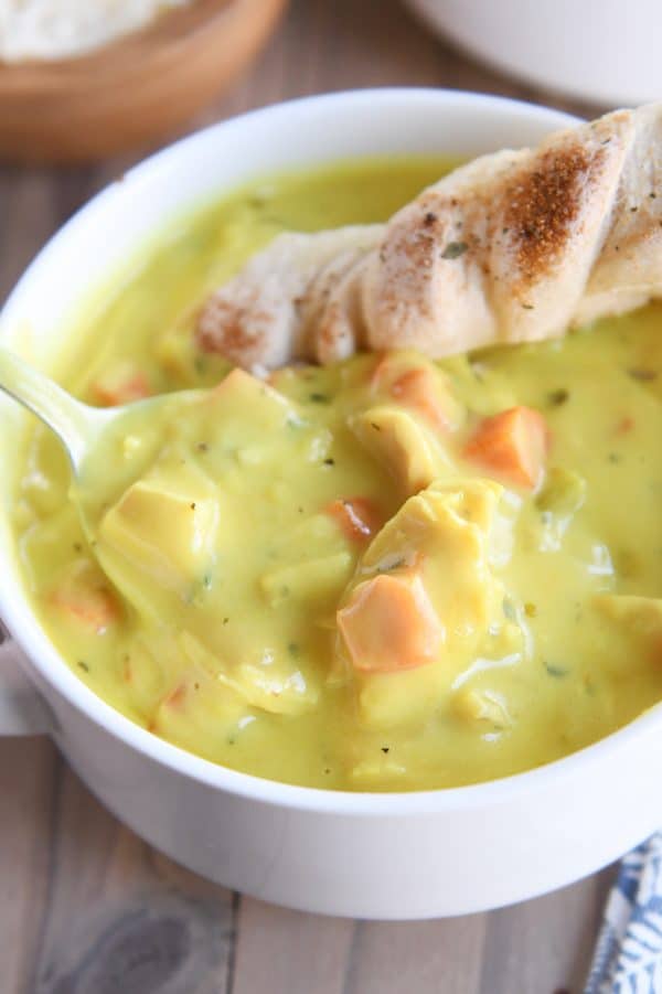 creamy chicken soup in white bowl with spoon and breadstick