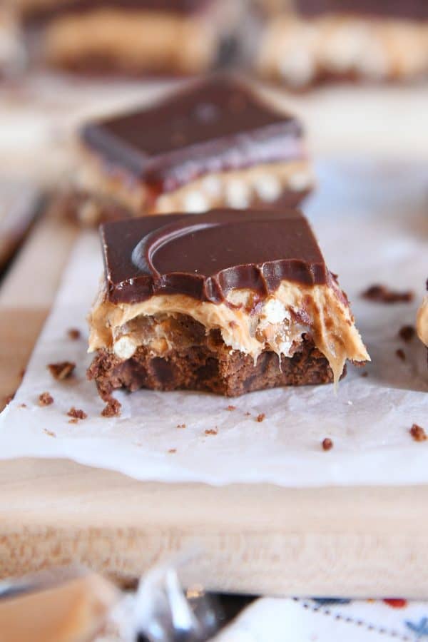 peanut butter pretzel caramel chocolate bar on piece of white parchment paper with bite taken out