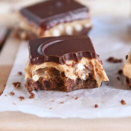 peanut butter pretzel caramel chocolate bar on piece of white parchment paper with bite taken out