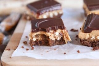 peanut butter pretzel caramel chocolate bar on piece of white parchment paper with bite taken out