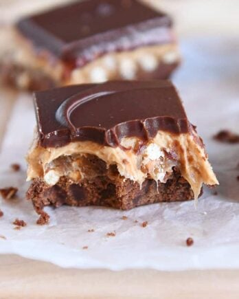 peanut butter pretzel caramel chocolate bar on piece of white parchment paper with bite taken out