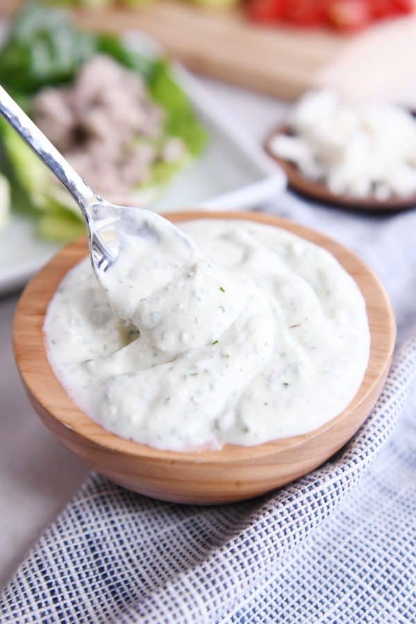 Spoon in wooden bowl filled with mint feta dressing.