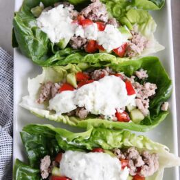 three greek lettuce wraps on white tray with cucumbers, tomatoes, with feta mint dressing