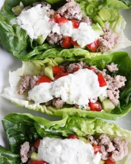 three greek lettuce wraps on white tray with cucumbers, tomatoes, with feta mint dressing