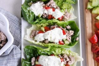 three greek lettuce wraps on white tray with cucumbers, tomatoes, with feta mint dressing