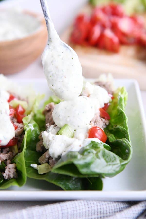 Drizzling feta dressing on greek lettuce wraps on white tray.