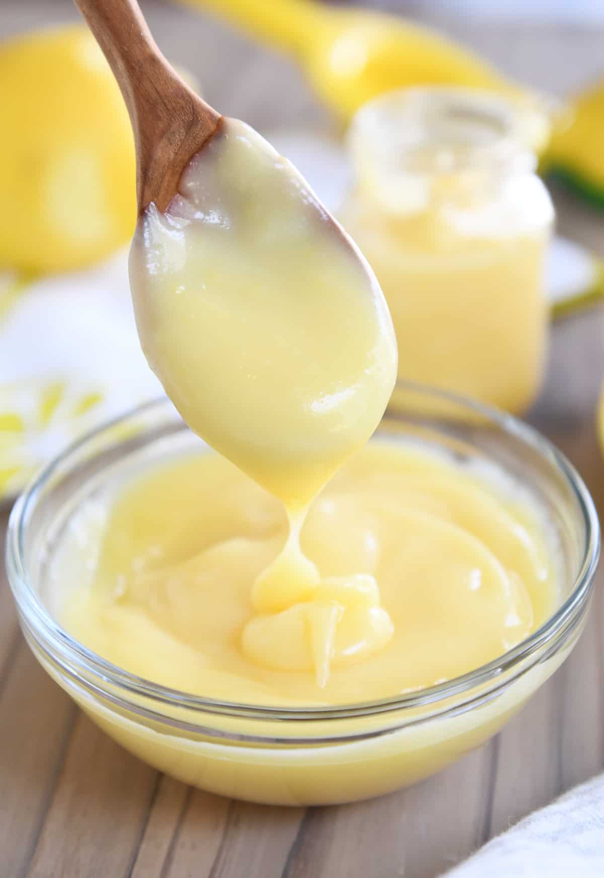 Wooden spoon dropping lemon curd into glass bowl.