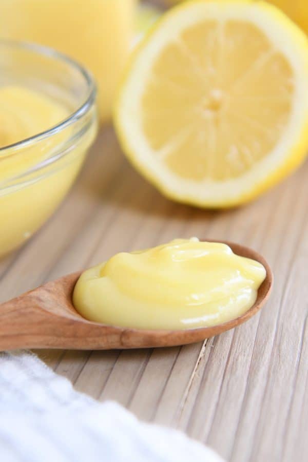 Wooden spoon with lemon curd on wood board.