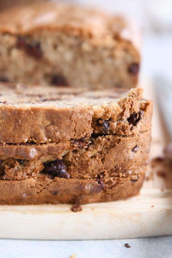 Three slices of peanut butter banana bread stacked on wood cutting board.