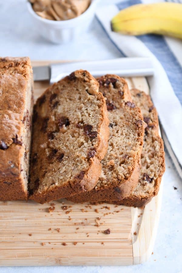 Slices from loaf of peanut butter banana bread on wood cutting board.