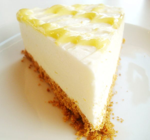 Slice of lemon cheesecake with lemon curd drizzle on top on a white plate.