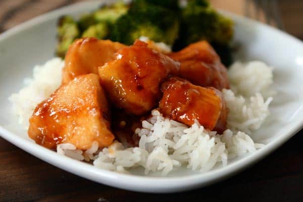 White rice and sticky bourbon chicken with a side of broccoli on a white plate.