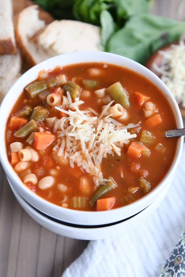 Minestrone soup in two stacked white bowls with parmesan cheese.