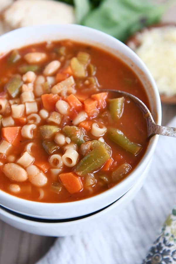 Spoon in bowl of classic minestrone soup in two stacked white bowls.