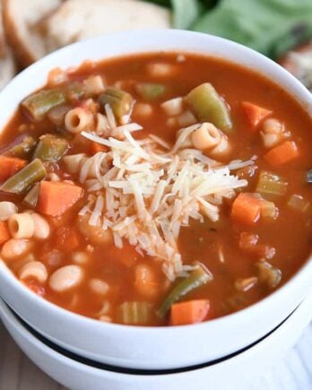 minestrone soup in two stacked white bowls with parmesan cheese