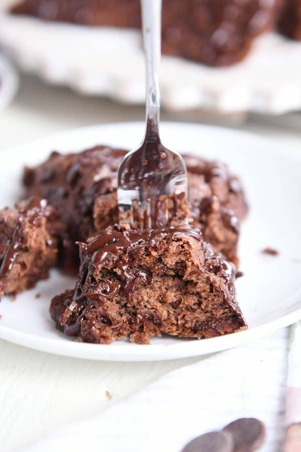 Fork scooping piece from chocolate scone on white plate.