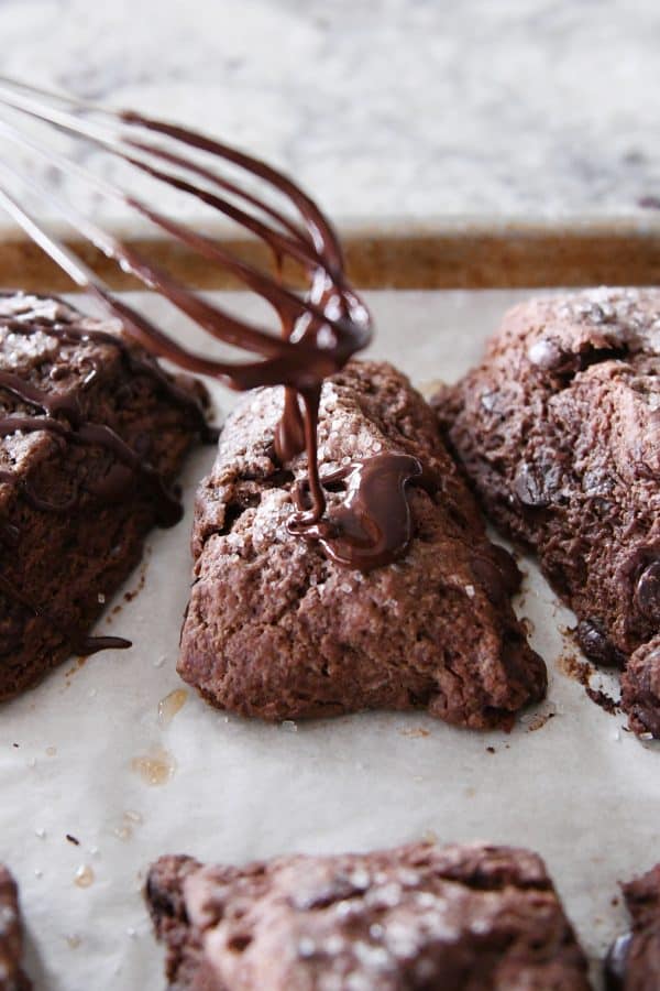 Drizzling glaze from whisk on to chocolate scones.