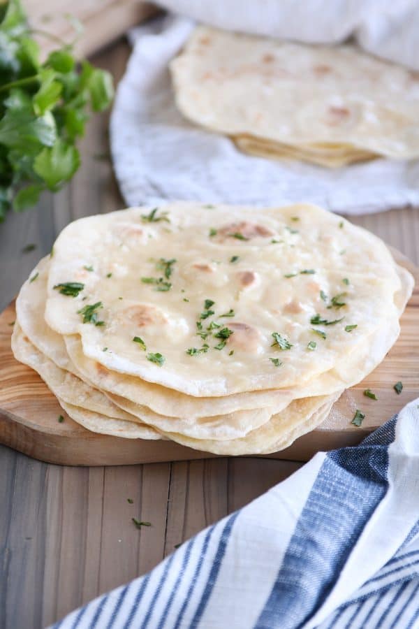 Stack of cooked yogurt flatbreads on wood cutting board sprinkled with parsley.