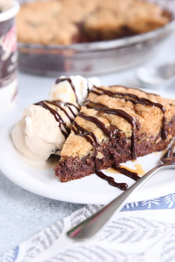 Slice of brookie pie on white plate with fork and ice cream.