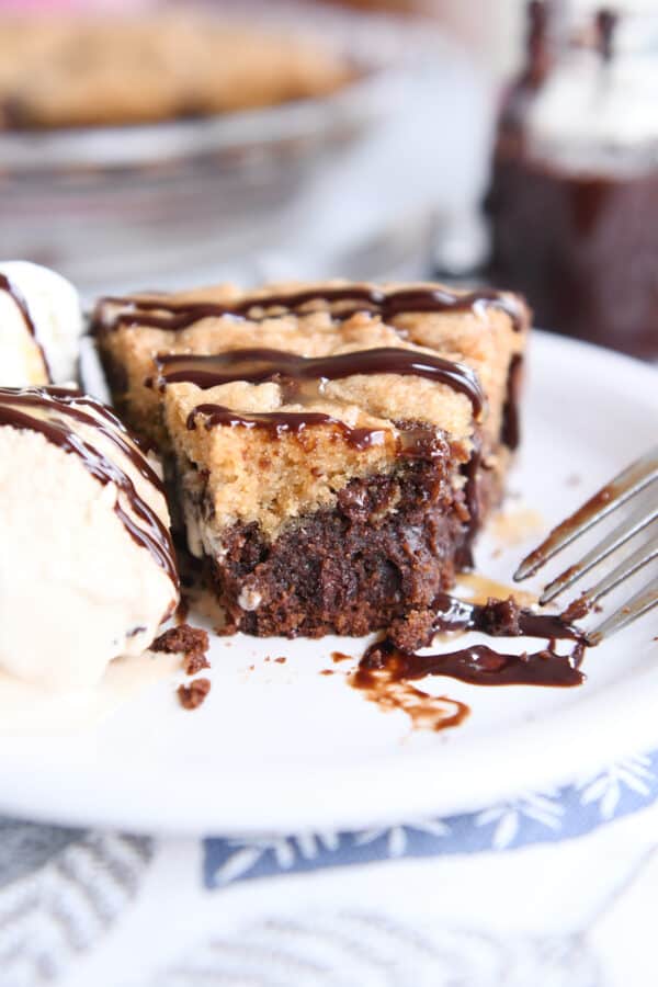 Piece of brookie pie with bite taken out on white plate with ice cream.