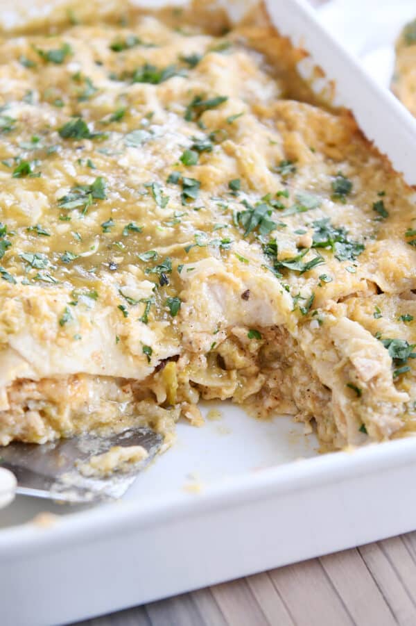 Chicken enchilada casserole in white pan with serving spoon.