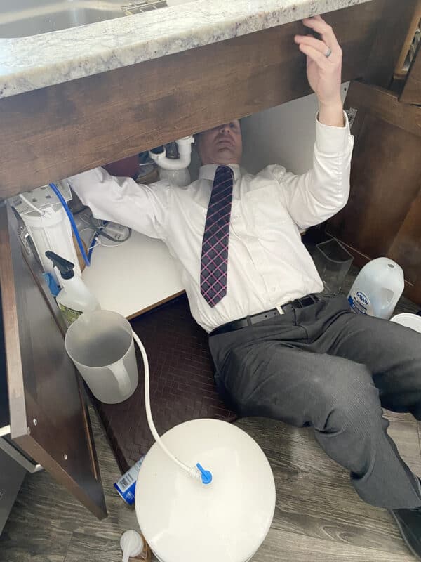 man fixing underneath sink in shirt and tie