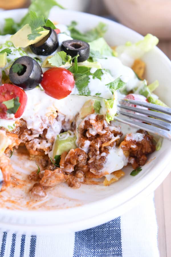 White bowl filled with corn chips, taco meat and taco toppings.