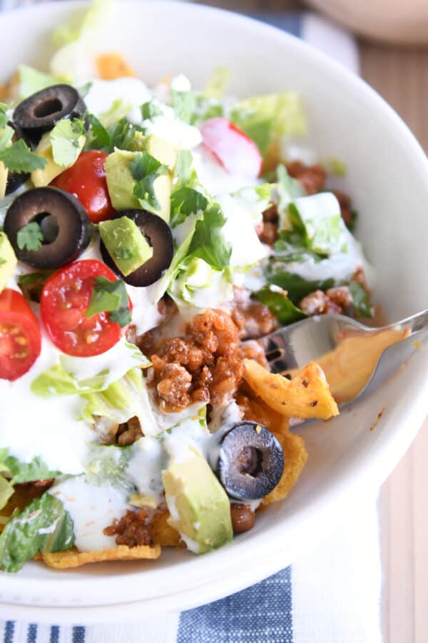 White bowl filled with corn chips, taco meat and taco toppings.