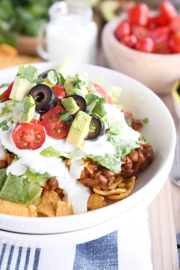 Floating taco bowls in white bowl with lettuce, tomatoes and olives.