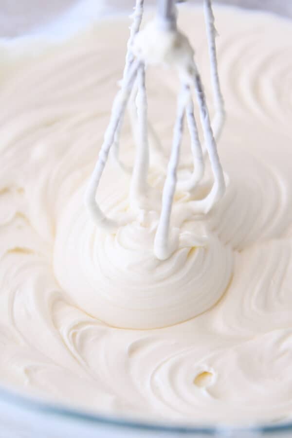 Whipping cheesecake batter in glass bowl with electric hand mixer.