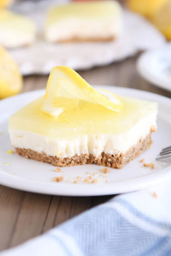 Square of lemon white chocolate cream bar on white plate with bite taken out.