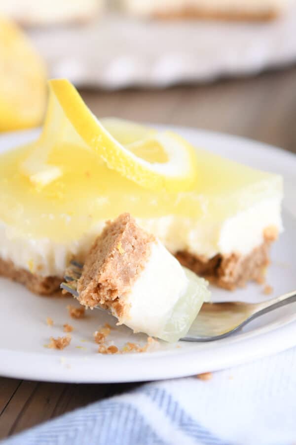 Square of lemon white chocolate cream bars on white plate with bite on fork.