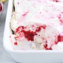 layered angel food cake, raspberries and whipped cream in white baking dish with scoop taken out