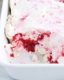 layered angel food cake, raspberries and whipped cream in white baking dish with scoop taken out