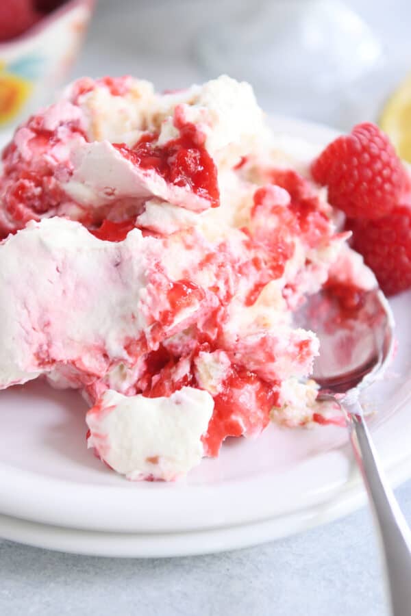 Scoop of raspberry and cream angel food cake dessert on white plate with spoon.