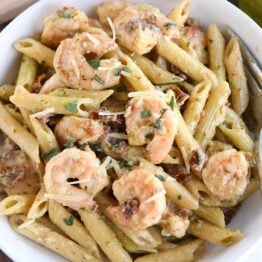 pasta with shrimp, parmesan and sun-dried tomatoes in white bowl with fork