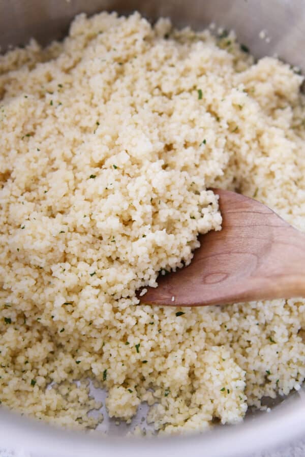 Spoon scooping out cooked couscous from a bowl. 