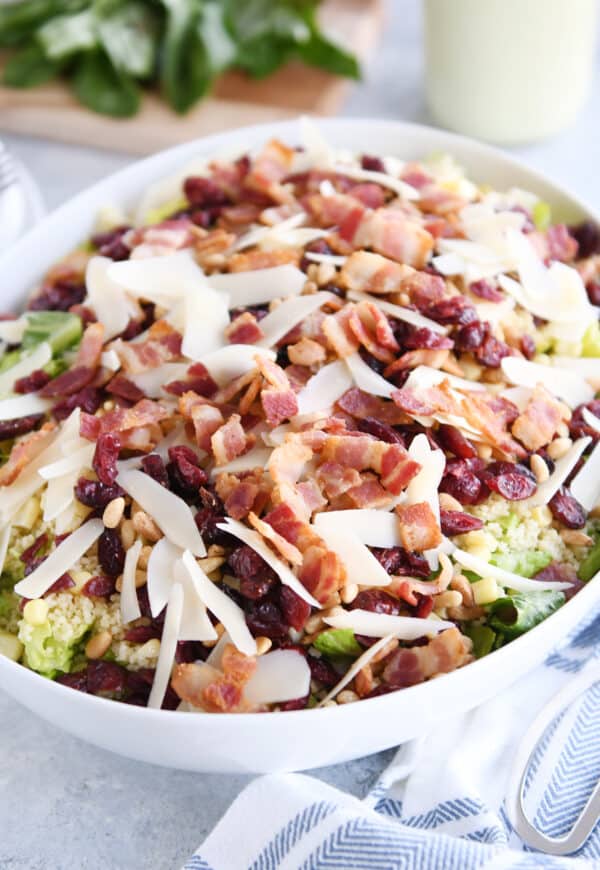 White serving bowl with romaine lettuce, bacon, parmesan, craisins, and pine nuts.