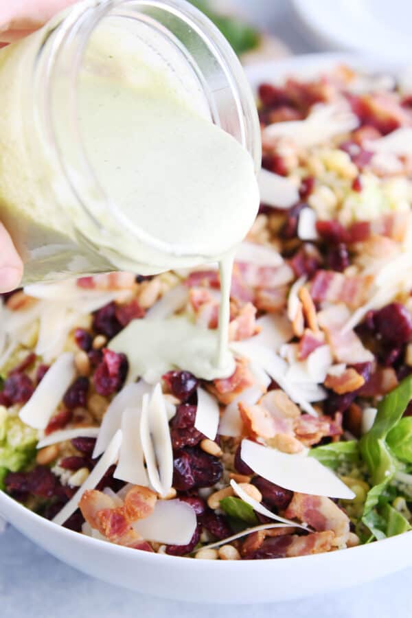 Pouring fresh basil dressing over couscous green salad.