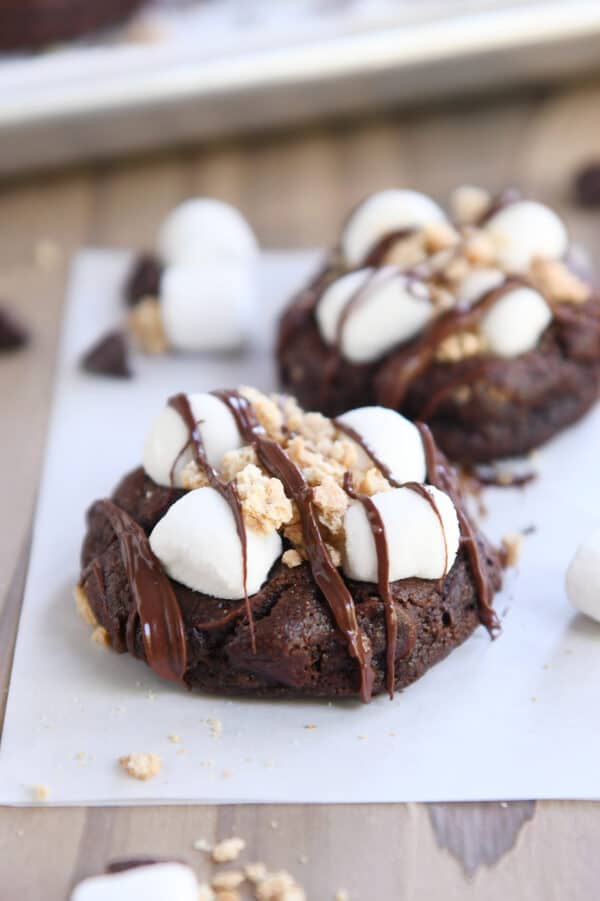 Two chocolate s'mores cookies on white parchment paper.