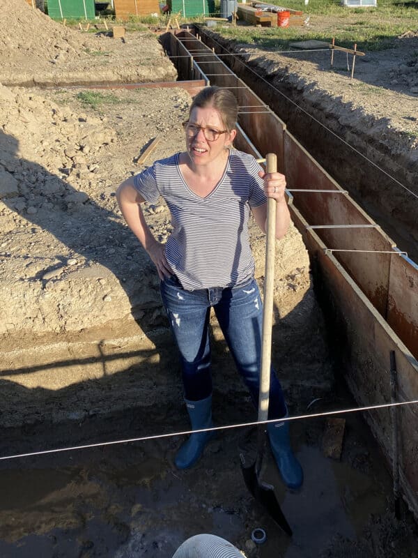 woman standing in mud filled trench with shovel