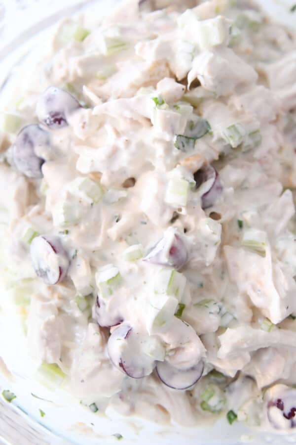 Chicken salad ingredients with creamy dressing in glass bowl.
