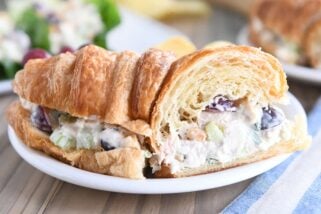 chicken salad sandwich on croissant cut in half on white plate with other half sandwich