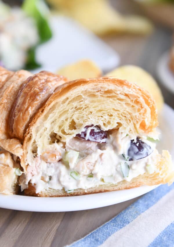 Chicken salad sandwich on croissant cut in half on white plate.