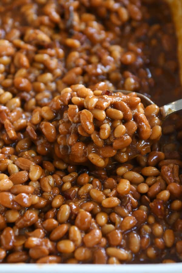 Scooping spoon in pan of saucy baked beans.