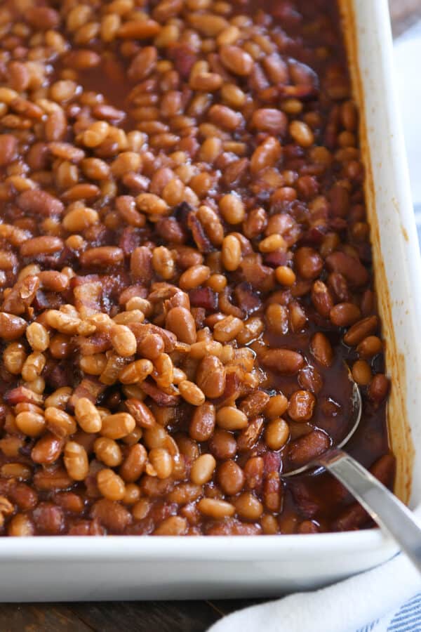 serving spoon in corner of white pan with saucy baked beans